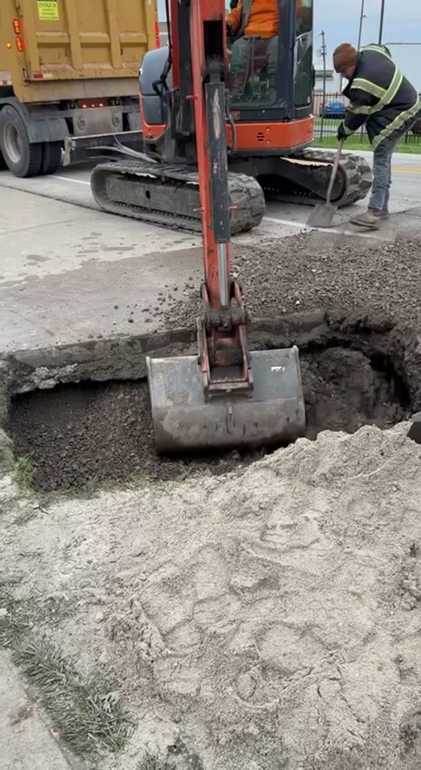 Mini excavator and crew performing road cut excavation